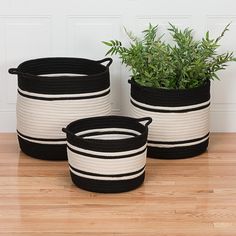 three black and white baskets with plants in them on a wooden floor next to a wall