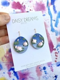 a pair of earrings with water lilies painted on the front and back of them