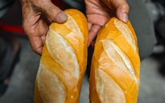 two people holding long loafs of bread in their hands, with one person's hand on top of them