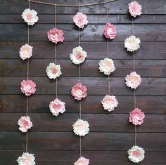 pink and white paper flowers are hanging from a string on a wooden wall with strings