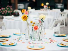 the table is set with flowers in vases, plates and napkins on it