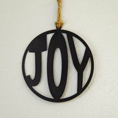 a black ornament with the word joy hanging from a rope on a white wall