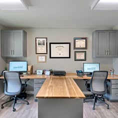 an office with two desks and three computers on top of each desk in front of gray cabinets