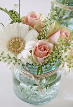 two mason jars filled with flowers and greenery on a white tablecloth covered table