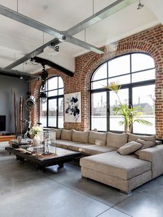 a living room with large windows and couches in front of the window is a brick wall