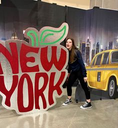 a woman standing next to a giant sign that says new york in front of a taxi