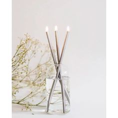 three candles are lit in a glass vase with flowers behind it on a white surface