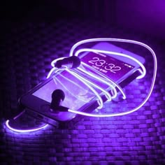 a cell phone hooked up to a charger that is glowing in the dark with neon lights