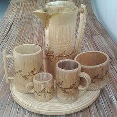 a pitcher and four mugs on a wooden tray with wicker mating around it