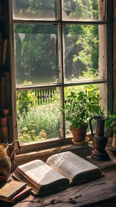 an open book sitting on top of a wooden table next to a window filled with plants