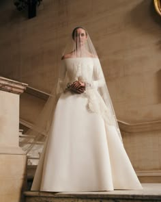 a woman in a white wedding dress standing on stairs with her veil over her head