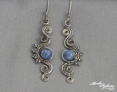 the earrings are made with wire and blue glass beads on silver earwires, sitting on a gray background