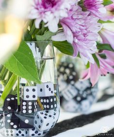 a vase filled with lots of black and white dice next to pink flowers on top of a table