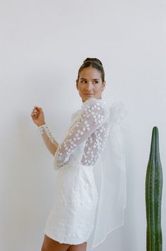 a woman standing next to a cactus wearing a white dress and holding her fist up