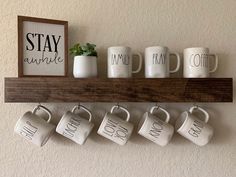 coffee mugs are hung on a shelf with the words stay awhile