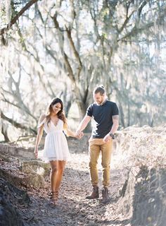 a man and woman holding hands while walking through the woods