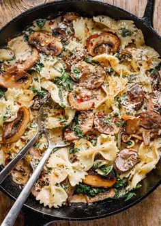 a skillet filled with pasta, mushrooms and spinach on top of a wooden table