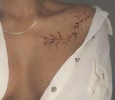 a woman with a tattoo on her chest is wearing a white shirt and gold necklace