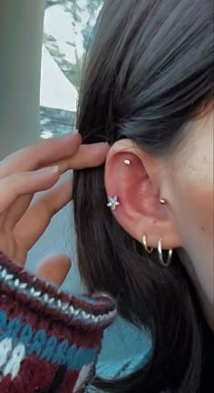 a woman is holding her ear up to the side with two piercings on it