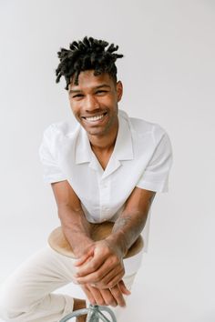 a man with dreadlocks sitting on top of a stool smiling at the camera