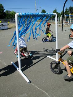 three children riding bikes in an outdoor play area with blue streamers on the poles