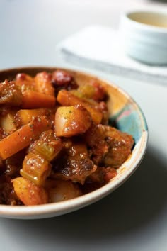 a close up of a bowl of food on a table with a cup in the background