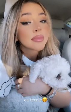 a woman holding a small white dog in her lap while sitting in the back seat of a car