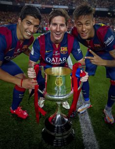 two soccer players are posing with the trophy in front of him and another player is smiling