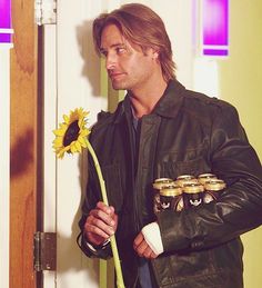 a man in leather jacket holding a sunflower next to some jars and a door