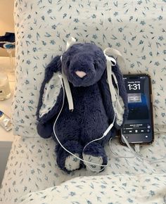 a blue stuffed animal sitting on top of a bed next to an ipod and headphones