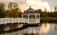 a white gazebo sitting on top of a lake next to a wooden bridge over water