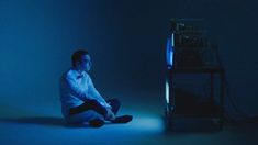 a man sitting on the floor in front of a computer monitor with blue light coming from behind him