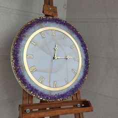 a purple and gold clock sitting on top of a wooden easel next to a wall