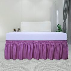 a white bed with purple ruffled bedskirt