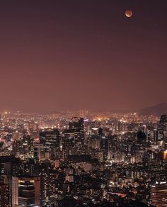 the city skyline is lit up at night with moon in the sky and lights on