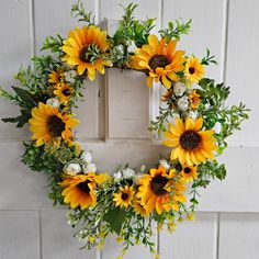 a wreath with sunflowers and greenery hanging on a white painted door frame