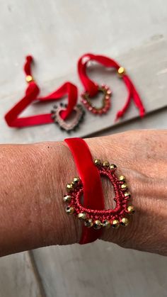 a woman's arm is adorned with red ribbon and gold beaded bracelets