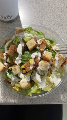 a salad with croutons and dressing in a glass bowl next to a coffee cup