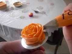 someone is holding an orange rose on top of a small cupcake with icing