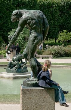 a woman sitting on top of a stone bench next to a statue in a park