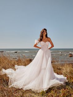 a woman in a white wedding dress standing on the beach with her hands on her hips