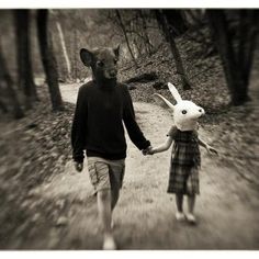 a man and woman walking down a path holding hands with a rabbit mask on their head