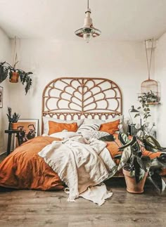 a bed with an orange comforter and some potted plants on the floor next to it