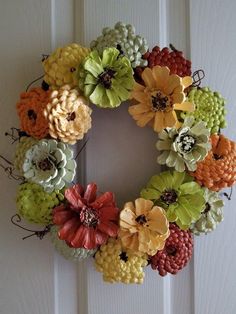 a wreath made out of pine cones and flowers on a white door frame with the words happy holidays written below it