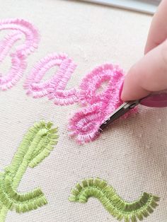 someone is doing something with pink and green thread on the fabric that has been embroidered onto