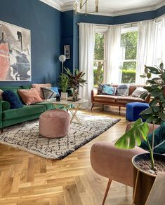 a living room with blue walls and wooden floors, pink velvet chairs, green couches and potted plants