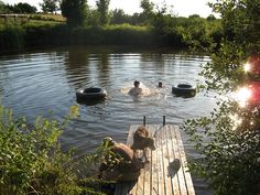 some people are swimming in the water and one is on a dock with two dogs