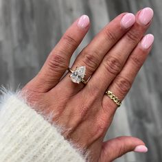 a woman's hand wearing a gold ring with a pear shaped diamond on it