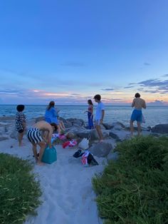 several people are standing on the beach at sunset