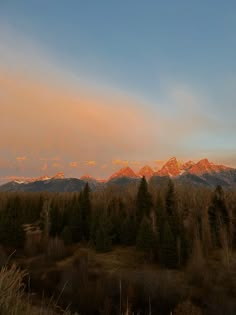 the sun is setting over mountains and trees